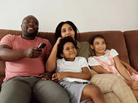 Família sentada no sofá, com controle remoto nas mãos.