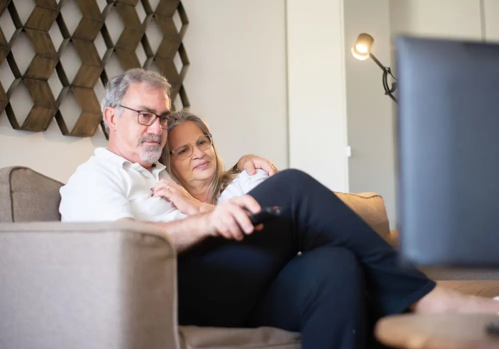 Casal em casa acompanhando a programação na sala de estar